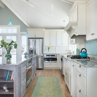 Large beach style kitchen pantry designs - Example of a large coastal l-shaped light wood floor kitchen pantry design in Providence with a farmhouse sink, recessed-panel cabinets, white cabinets, granite countertops, blue backsplash, glass tile backsplash, stainless steel appliances and an island