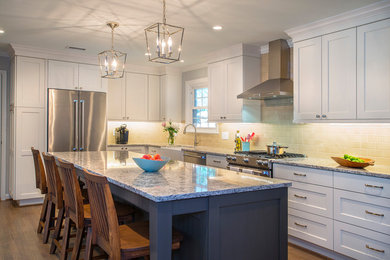 Photo of a large transitional l-shaped eat-in kitchen in Charleston with a farmhouse sink, shaker cabinets, white cabinets, beige splashback, subway tile splashback, stainless steel appliances, medium hardwood floors, with island, brown floor and quartz benchtops.