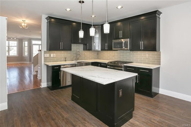 Eat-in kitchen - mid-sized contemporary u-shaped porcelain tile and brown floor eat-in kitchen idea in New York with a farmhouse sink, shaker cabinets, black cabinets, quartzite countertops, gray backsplash, subway tile backsplash, stainless steel appliances, an island and white countertops