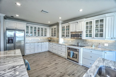 Large beach style l-shaped porcelain tile and brown floor kitchen photo in Tampa with a double-bowl sink, raised-panel cabinets, white cabinets, granite countertops, beige backsplash, matchstick tile backsplash, stainless steel appliances and an island