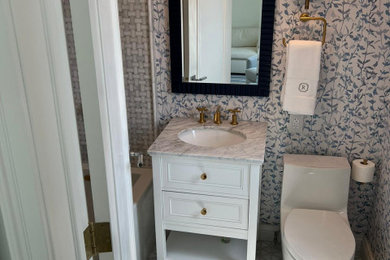 Inspiration for a transitional master gray tile and marble tile marble floor, white floor, single-sink and wallpaper bathroom remodel in New York with recessed-panel cabinets, white cabinets, a one-piece toilet, blue walls, a drop-in sink, marble countertops, gray countertops and a freestanding vanity