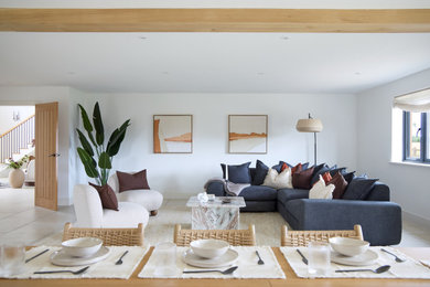 This is an example of a contemporary formal open plan living room in Cambridgeshire with white walls, porcelain flooring, no fireplace, no tv, beige floors and exposed beams.
