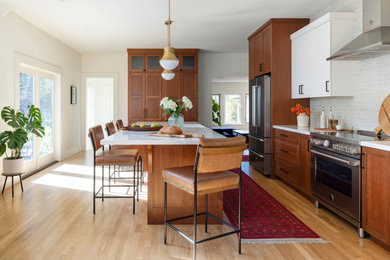 Inspiration for a mid-sized craftsman l-shaped light wood floor and beige floor enclosed kitchen remodel in Other with a farmhouse sink, recessed-panel cabinets, wood countertops, green backsplash, ceramic backsplash, stainless steel appliances, an island and brown countertops