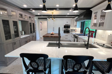 Photo of a large modern l-shaped kitchen/diner in New York with a submerged sink, glass-front cabinets, white cabinets, engineered stone countertops, white splashback, engineered quartz splashback, integrated appliances, porcelain flooring, an island, beige floors, white worktops and exposed beams.
