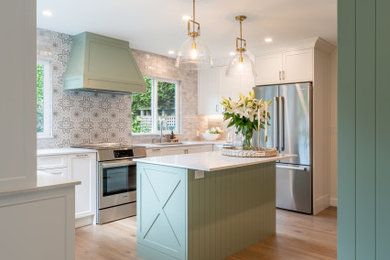 Photo of a medium sized traditional u-shaped open plan kitchen in Vancouver with a submerged sink, shaker cabinets, green cabinets, engineered stone countertops, grey splashback, ceramic splashback, stainless steel appliances, light hardwood flooring, an island and white worktops.
