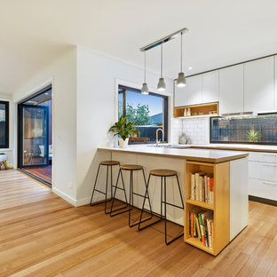 Создайте стильный интерьер: маленькая п-образная кухня-гостиная в современном стиле с накладной раковиной, фасадами с выступающей филенкой, белыми фасадами, мраморной столешницей, белым фартуком, фартуком из керамической плитки, техникой из нержавеющей стали, светлым паркетным полом, островом, желтым полом и белой столешницей - последний тренд