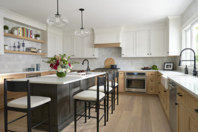 Example of a transitional light wood floor eat-in kitchen design in New York with a farmhouse sink, recessed-panel cabinets, quartzite countertops, white backsplash, stainless steel appliances, an island and white countertops