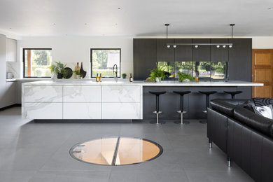 This is an example of an expansive contemporary grey and black l-shaped open plan kitchen in Sussex with flat-panel cabinets, dark wood cabinets, engineered stone countertops, multi-coloured splashback, engineered quartz splashback, black appliances, an island, grey floors, multicoloured worktops and an integrated sink.
