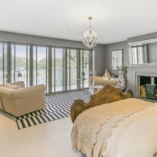 Mittelgroßes Klassisches Schlafzimmer mit grauer Wandfarbe, Teppichboden, Kaminofen und beigem Boden in London