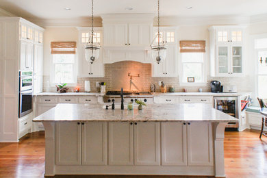 Inspiration for a large arts and crafts l-shaped eat-in kitchen in Atlanta with shaker cabinets, an undermount sink, white cabinets, granite benchtops, beige splashback, subway tile splashback, stainless steel appliances, medium hardwood floors and with island.