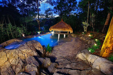 This is an example of a mid-sized tropical front yard custom-shaped natural pool in Brisbane with a water slide and stamped concrete.
