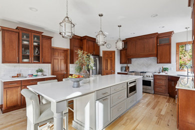 Eat-in kitchen - mid-sized transitional u-shaped light wood floor and brown floor eat-in kitchen idea in Minneapolis with an undermount sink, recessed-panel cabinets, medium tone wood cabinets, quartz countertops, white backsplash, ceramic backsplash, stainless steel appliances, an island and white countertops