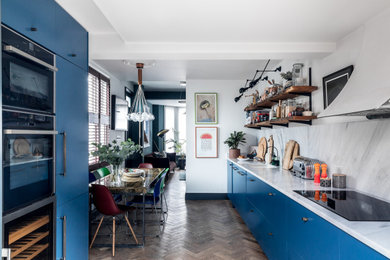 Design ideas for a small eclectic galley eat-in kitchen in London with an integrated sink, flat-panel cabinets, blue cabinets, marble benchtops, white splashback, marble splashback, stainless steel appliances, medium hardwood floors, no island, brown floor and white benchtop.