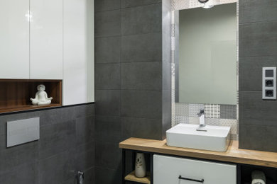 Industriell inredning av ett litet brun brunt badrum med dusch, med öppna hyllor, skåp i mellenmörkt trä, våtrum, en vägghängd toalettstol, svart och vit kakel, porslinskakel, grå väggar, klinkergolv i porslin, ett nedsänkt handfat, träbänkskiva, grått golv och dusch med gångjärnsdörr