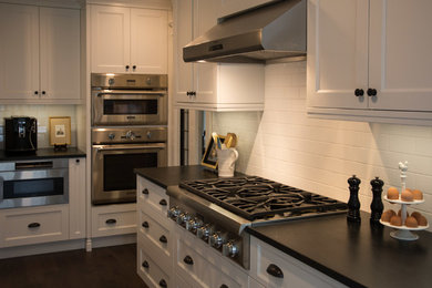 Kitchen - mid-sized traditional u-shaped dark wood floor kitchen idea in Toronto with an undermount sink, shaker cabinets, white cabinets, soapstone countertops, white backsplash, ceramic backsplash, stainless steel appliances and an island