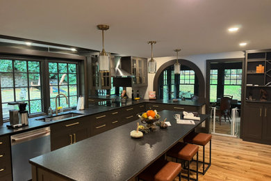 1950s l-shaped light wood floor and brown floor eat-in kitchen photo in Philadelphia with an undermount sink, recessed-panel cabinets, black cabinets, granite countertops, multicolored backsplash, mirror backsplash, stainless steel appliances, an island and black countertops