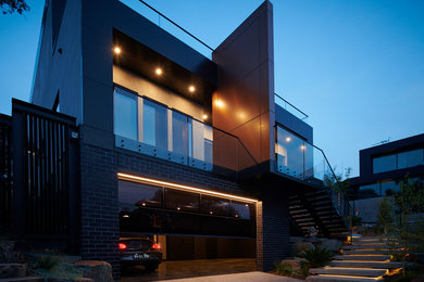 Large modern three-storey black house exterior in Melbourne with metal siding, a flat roof and a metal roof.