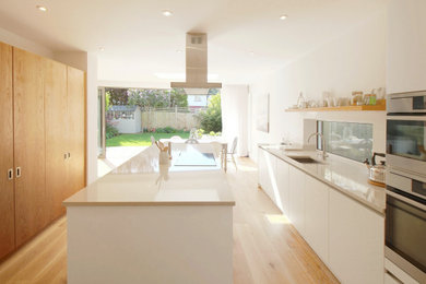 This is an example of a large modern single-wall open plan kitchen in Sussex with flat-panel cabinets, beige cabinets, solid surface benchtops, panelled appliances, medium hardwood floors, with island and beige benchtop.
