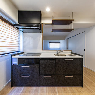 Modern single-wall open plan kitchen in Tokyo with black cabinets, white splashback, plywood floors, with island, brown floor and wallpaper.
