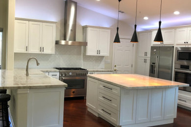 This is an example of a modern u-shaped open plan kitchen in San Francisco with a built-in sink, raised-panel cabinets, white cabinets, quartz worktops, white splashback, stainless steel appliances, multiple islands, brown floors, grey worktops and a vaulted ceiling.