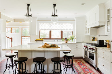 Photo of a traditional l-shaped kitchen in Boston with a farmhouse sink, shaker cabinets, white cabinets, white splashback, subway tile splashback, dark hardwood floors and with island.