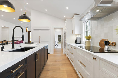 Open concept kitchen - mid-sized contemporary l-shaped light wood floor, brown floor and vaulted ceiling open concept kitchen idea in Calgary with a single-bowl sink, shaker cabinets, white cabinets, quartz countertops, white backsplash, ceramic backsplash, paneled appliances, an island and white countertops