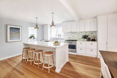 Bild på ett stort funkis vit linjärt vitt kök med öppen planlösning, med skåp i shakerstil, vita skåp, marmorbänkskiva, grönt stänkskydd, stänkskydd i tunnelbanekakel, rostfria vitvaror, mellanmörkt trägolv, en köksö och brunt golv