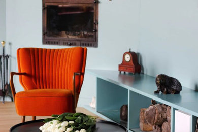 Photo of a large midcentury formal open concept living room in London with green walls, medium hardwood floors, a corner fireplace, a plaster fireplace surround, a wall-mounted tv and brown floor.