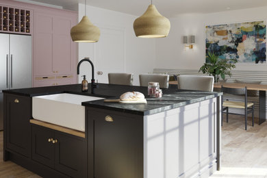 Photo of a medium sized contemporary kitchen/diner in Other with a belfast sink, shaker cabinets, black cabinets, quartz worktops, stainless steel appliances, light hardwood flooring, an island and black worktops.