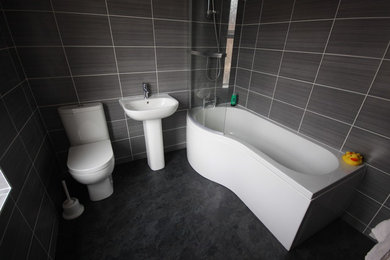 Modern inredning av ett mellanstort badrum för barn, med en toalettstol med separat cisternkåpa, grå kakel, keramikplattor, grå väggar, vinylgolv, ett piedestal handfat och svart golv