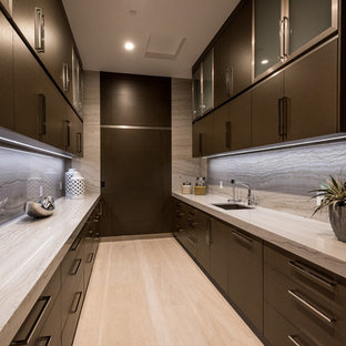 Zweizeilige, Große Moderne Küche mit Unterbauwaschbecken, flächenbündigen Schrankfronten, dunklen Holzschränken, Granit-Arbeitsplatte, Küchenrückwand in Grau, Rückwand aus Stein, Küchengeräten aus Edelstahl, Kalkstein, Kücheninsel, beigem Boden, Vorratsschrank und beiger Arbeitsplatte in Las Vegas