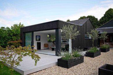 Photo of a medium sized and black contemporary bungalow rear house exterior in Gloucestershire with wood cladding and board and batten cladding.