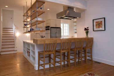 Inspiration for a modern medium tone wood floor eat-in kitchen remodel in Raleigh with a farmhouse sink, flat-panel cabinets, white cabinets, quartzite countertops and stainless steel appliances