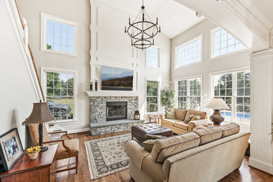 Inspiration for a large transitional enclosed medium tone wood floor and brown floor living room remodel in Philadelphia with white walls, a standard fireplace, a stone fireplace and a wall-mounted tv