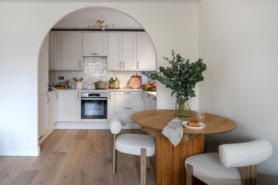 Design ideas for a medium sized classic cream and black u-shaped open plan kitchen in London with a built-in sink, shaker cabinets, white cabinets, quartz worktops, white splashback, cement tile splashback, black appliances, light hardwood flooring, no island, beige floors and white worktops.