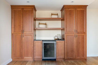 Inspiration for a transitional medium tone wood floor home bar remodel in Calgary with shaker cabinets, medium tone wood cabinets, granite countertops and black countertops