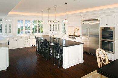 Large transitional u-shaped dark wood floor eat-in kitchen photo in Seattle with a farmhouse sink, white cabinets, white backsplash, stainless steel appliances, an island, shaker cabinets and marble countertops