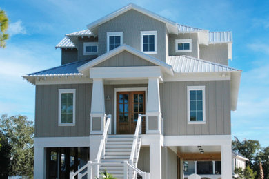 Example of a beach style gray three-story house exterior design with a hip roof and a metal roof