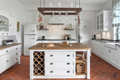 Eat-in kitchen - country galley brick floor and red floor eat-in kitchen idea in Other with a farmhouse sink, granite countertops, white backsplash, ceramic backsplash, white appliances, an island and black countertops