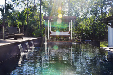 This is an example of a large tropical side yard rectangular infinity pool in Other with a hot tub and decking.
