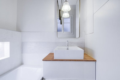 Aménagement d'une salle de bain principale classique de taille moyenne avec un placard à porte affleurante, des portes de placard blanches, une baignoire encastrée, un combiné douche/baignoire, WC suspendus, un carrelage beige, des carreaux de céramique, un mur blanc, un sol en carrelage de céramique, une vasque et un plan de toilette en bois.