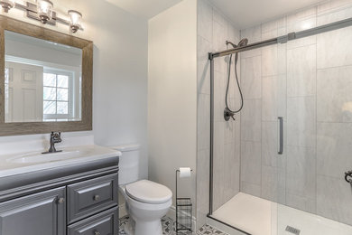Example of a mid-sized transitional 3/4 ceramic tile and multicolored floor bathroom design in Toronto with raised-panel cabinets, gray cabinets, a two-piece toilet, white walls, an integrated sink, quartz countertops and white countertops