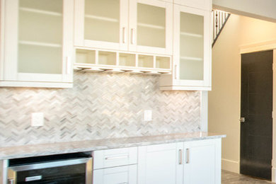 Inspiration for a small transitional single-wall medium tone wood floor and brown floor wet bar remodel in Calgary with shaker cabinets, white cabinets, marble countertops, gray backsplash and marble backsplash