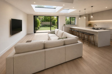This is an example of an open plan living room in Essex with white walls, light hardwood flooring, a wall mounted tv and brown floors.