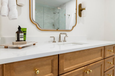 Example of a mid-sized classic white tile and porcelain tile porcelain tile and single-sink alcove shower design in New York with shaker cabinets, medium tone wood cabinets, a two-piece toilet, white walls, an undermount sink, quartz countertops, a hinged shower door, white countertops, a niche and a built-in vanity