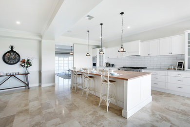 Photo of an expansive country kitchen in Sydney with a farmhouse sink, shaker cabinets, white cabinets, solid surface benchtops, white splashback, subway tile splashback, stainless steel appliances, travertine floors and with island.