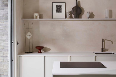 This is an example of a large scandi galley kitchen/diner in London with an integrated sink, flat-panel cabinets, beige cabinets, composite countertops, beige splashback, black appliances, concrete flooring, an island, grey floors and white worktops.