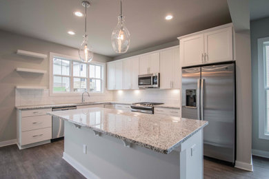 Example of a large cottage l-shaped vinyl floor and brown floor open concept kitchen design in Louisville with an undermount sink, recessed-panel cabinets, white cabinets, granite countertops, white backsplash, subway tile backsplash, stainless steel appliances, an island and multicolored countertops