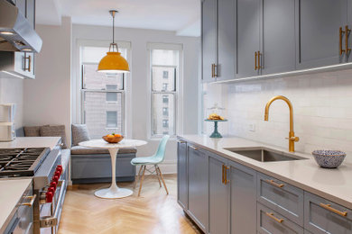ニューヨークにある高級な中くらいなトランジショナルスタイルのおしゃれなキッチン (アンダーカウンターシンク、落し込みパネル扉のキャビネット、青いキャビネット、クオーツストーンカウンター、白いキッチンパネル、大理石のキッチンパネル、シルバーの調理設備、淡色無垢フローリング、アイランドなし、茶色い床、白いキッチンカウンター、表し梁) の写真