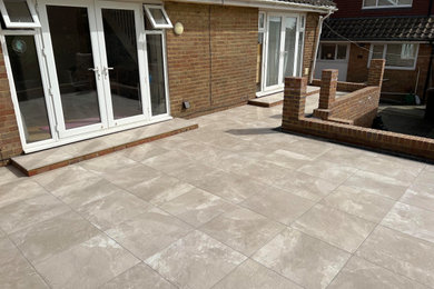 This is an example of a large modern back patio in Sussex with tiled flooring and no cover.